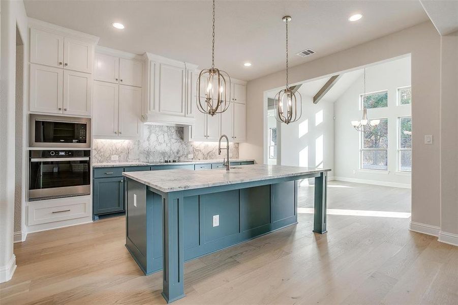 Kitchen featuring built in microwave, decorative light fixtures, white cabinets, oven, and an island with sink