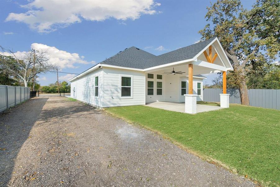 Rear view of house featuring a ceiling fan, a patio, roof with shingles, and driveway