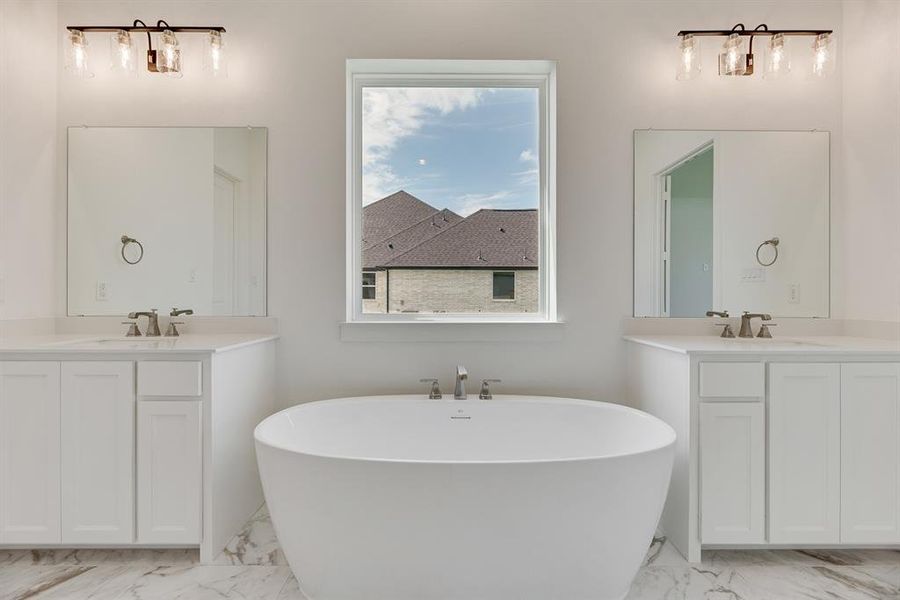 Bathroom featuring two vanities, light marble finish flooring, and a freestanding bath