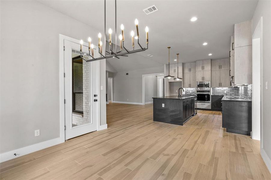 Kitchen with light wood-type flooring, pendant lighting, appliances with stainless steel finishes, a kitchen island with sink, and backsplash