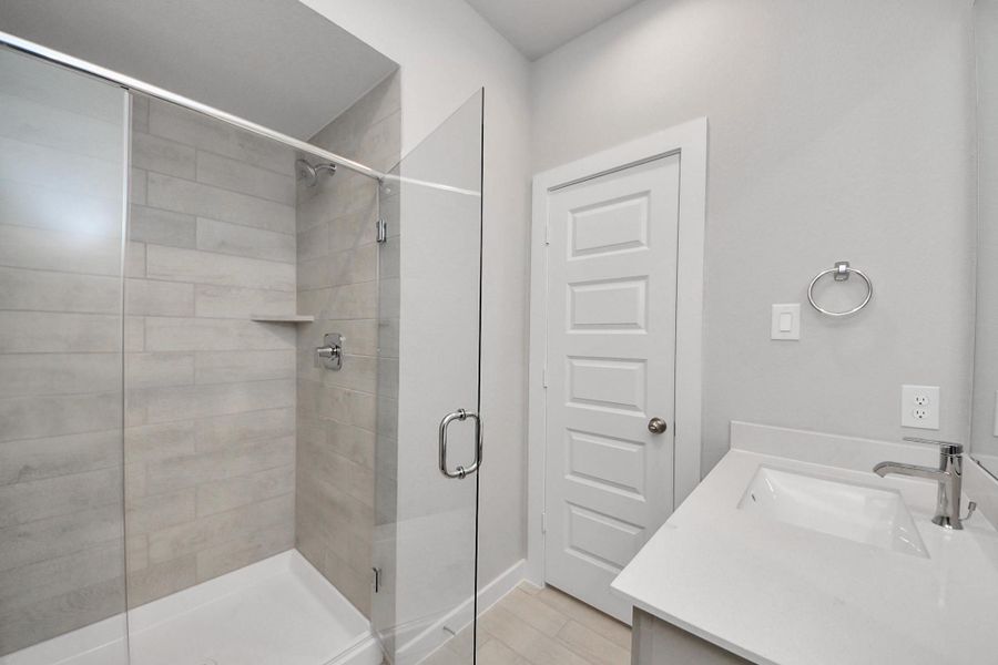 Secondary bath features tile flooring, walk-in shower with tile surround, light stained wood cabinets, beautiful light countertop. Sample photo of completed home with similar floor plan. Actual colors and selections may vary.