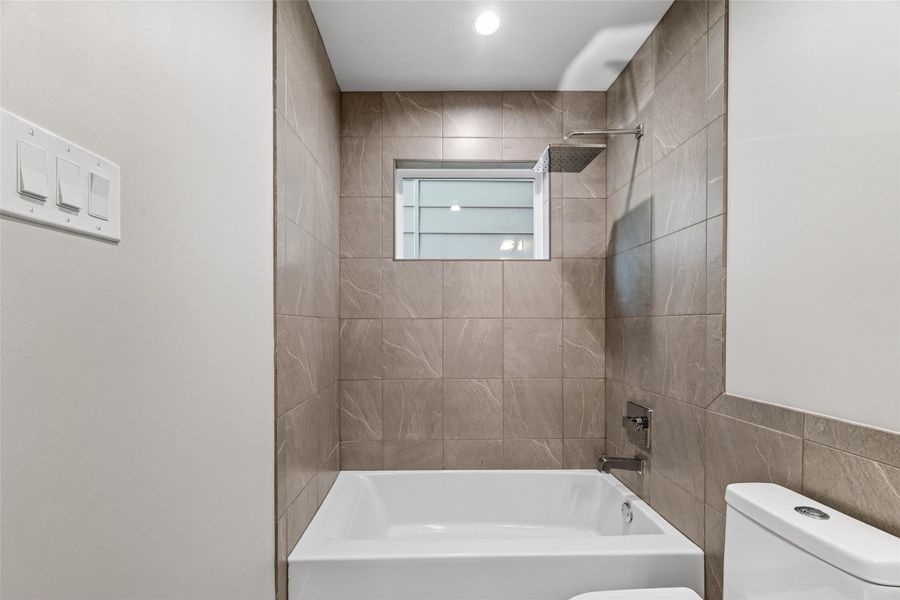 The first-floor full bath features a soaking tub and shower combination with a rain showerhead, set within full-height large-format tile surround. Refined finishes and recessed lighting give this ground-level bath a spa-like quality.