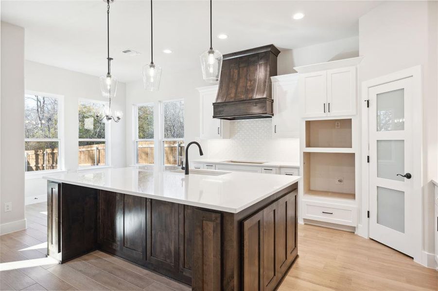 Kitchen with premium range hood, a kitchen island with sink, sink, decorative light fixtures, and white cabinetry