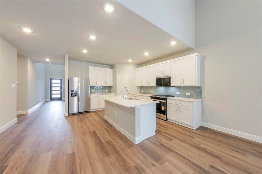 Kitchen with appliances with stainless steel finishes, white cabinets, an island with sink, backsplash, and recessed lighting Kitchen with appliances with stainless steel finishes, white cabinets, an island with sink, backsplash, and recessed lighting