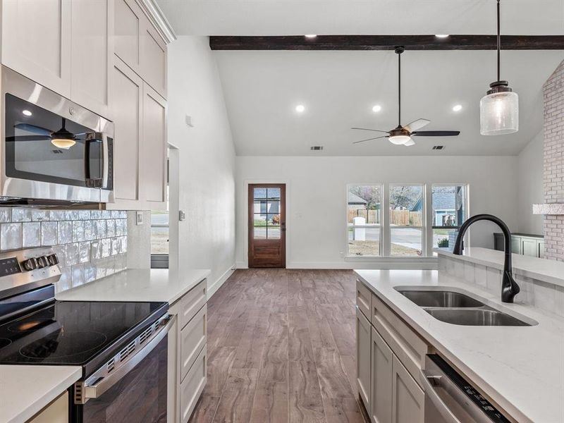 Kitchen featuring ceiling fan, beamed ceiling, light wood-style flooring, stainless steel appliances, and a sink