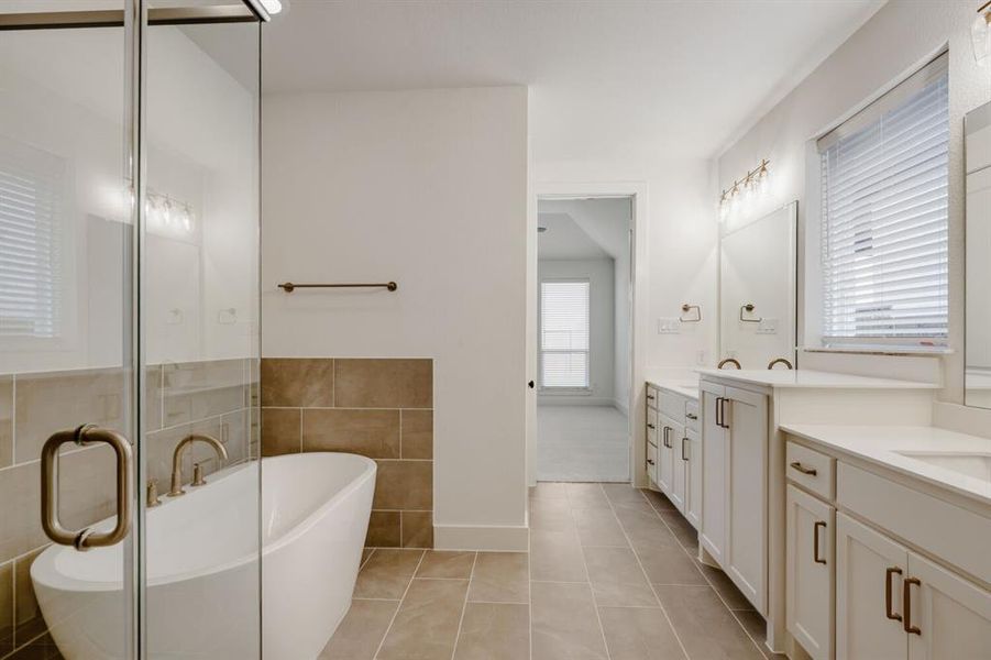 Bathroom featuring a freestanding tub, glass-enclosed shower, dual vanities with undermount sinks, tile flooring, and white cabinetry with dark hardware