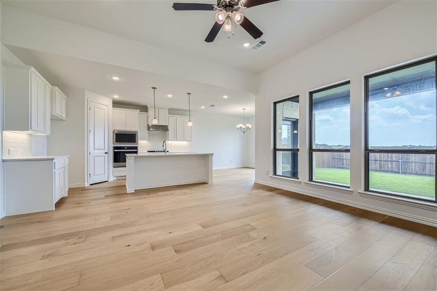 Kitchen with light hardwood / wood-style floors, white cabinetry, appliances with stainless steel finishes, an island with sink, and pendant lighting