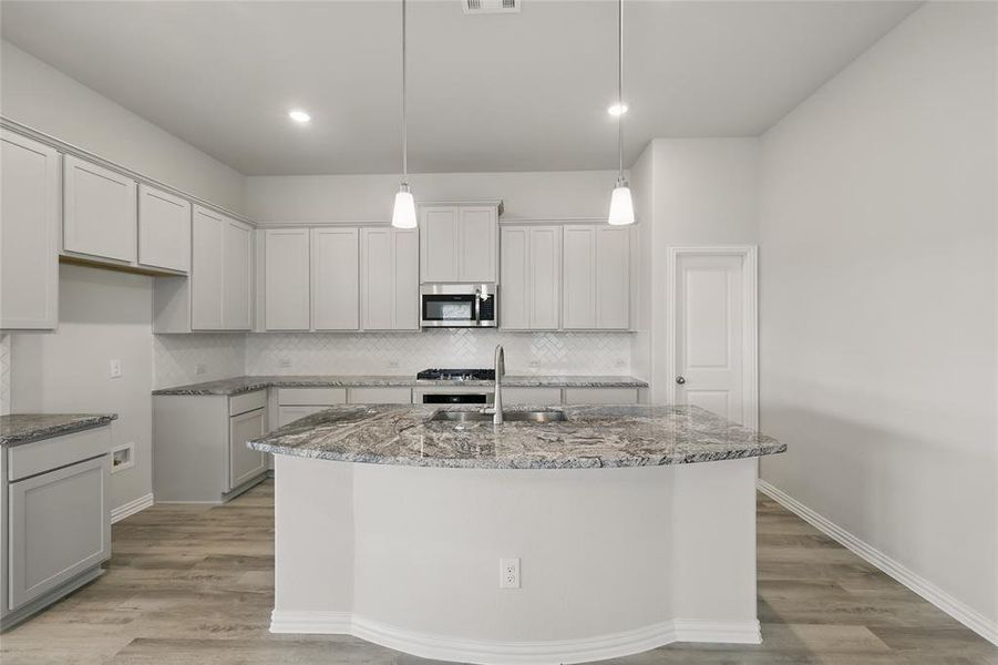 Kitchen featuring stainless steel microwave, stone counters, a sink, a center island with sink, and recessed lighting Kitchen featuring stainless steel microwave, stone counters, a sink, a center island with sink, and recessed lighting