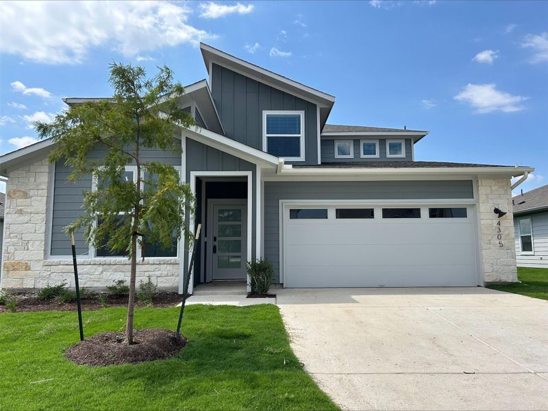 View of front of home with stone siding, board and batten siding, concrete driveway, a garage, and a front lawn
