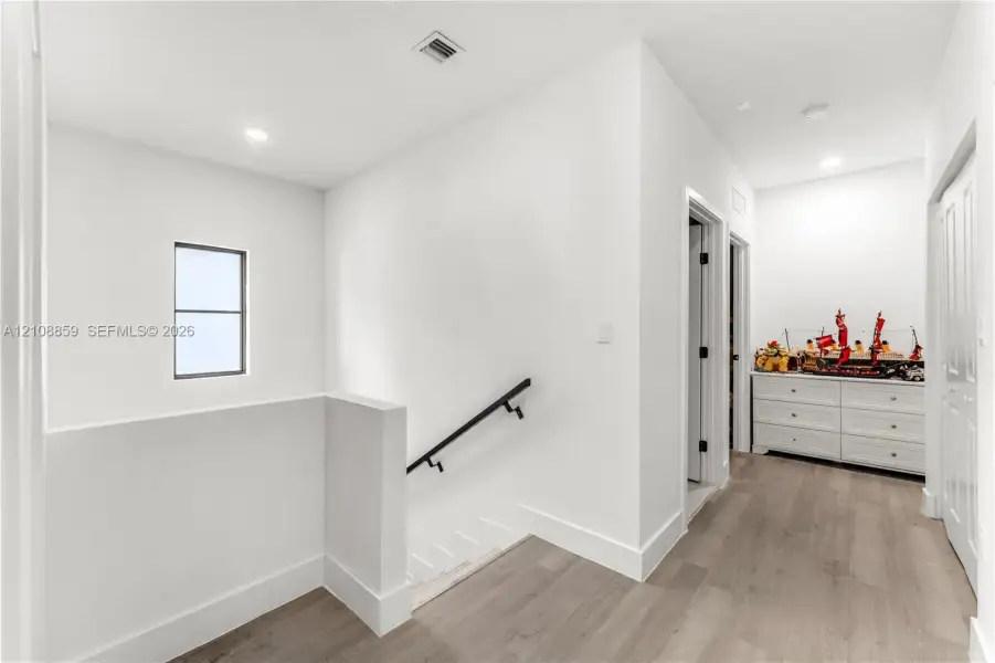 Interior hallway featuring wood-finish flooring, matte black handrail, recessed lighting, and multi-pane window