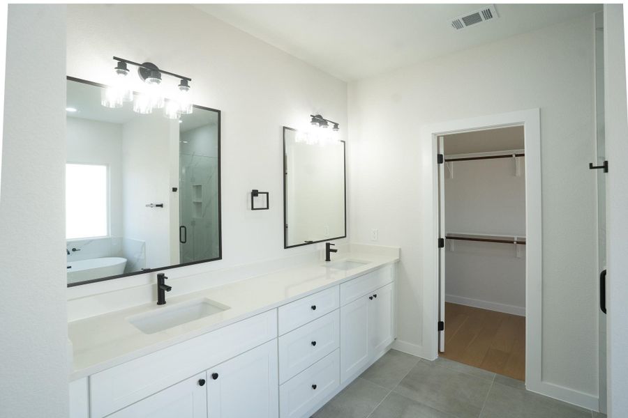 Bathroom with a stall shower, double vanity, a freestanding bath, a walk in closet, and light tile patterned floors