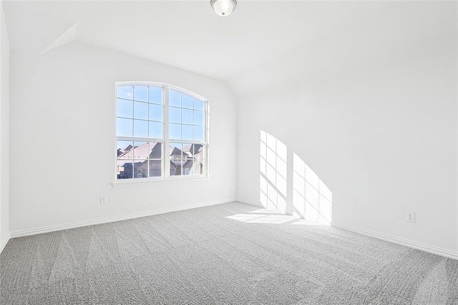 Carpeted spare room featuring vaulted ceiling