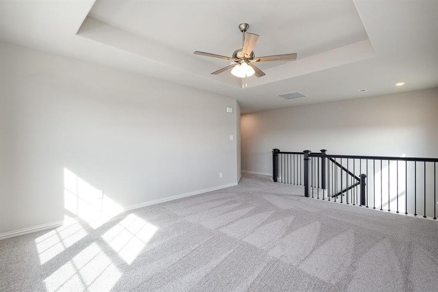 Unfurnished room with ceiling fan, light colored carpet, and a tray ceiling