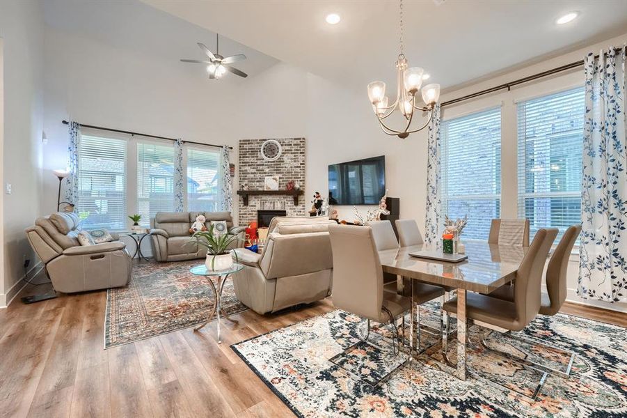 Dining area featuring a fireplace, ceiling fan with notable chandelier, high vaulted ceiling, and light hardwood / wood-style flooring