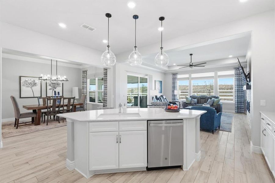 Kitchen with white cabinets, stainless steel dishwasher, hanging light fixtures, a center island with sink, and open floor plan