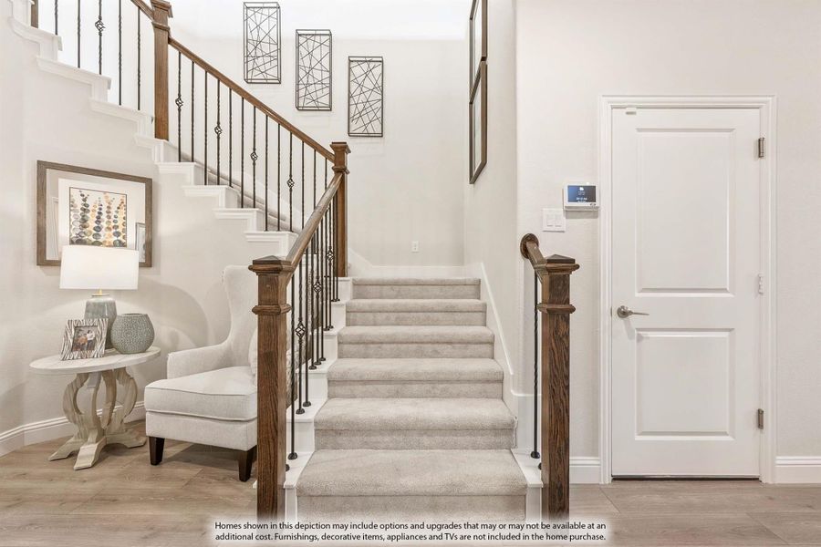 Carpeted staircase with wood newel posts and wrought iron balusters in a bright two-story entryway