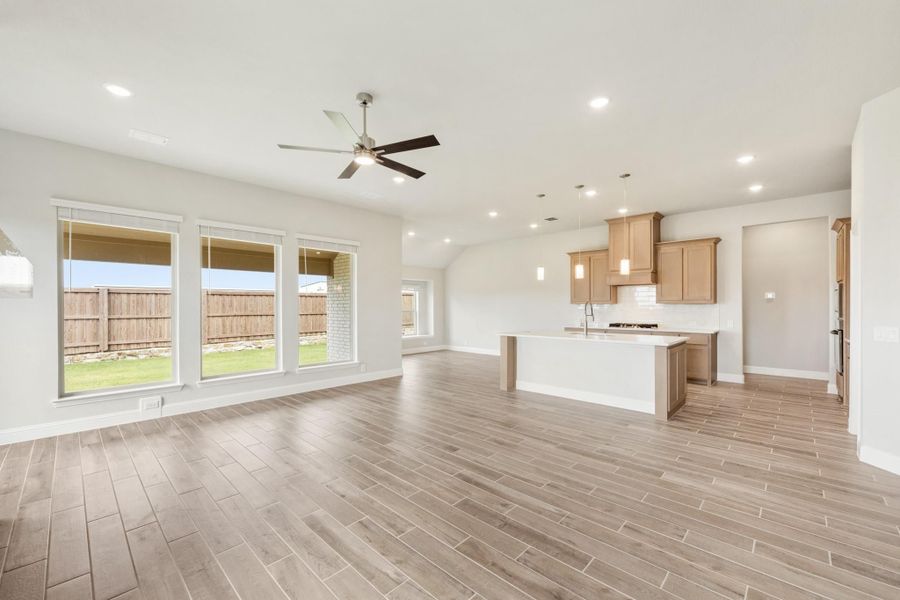 Open living area with wood-look tile floors, ceiling fan, and kitchen with island and tan cabinets visible in background