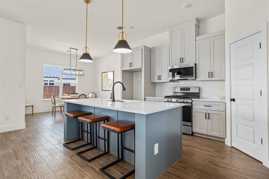Kitchen with tasteful backsplash, a center island with sink, pendant lighting, sink, and appliances with stainless steel finishes