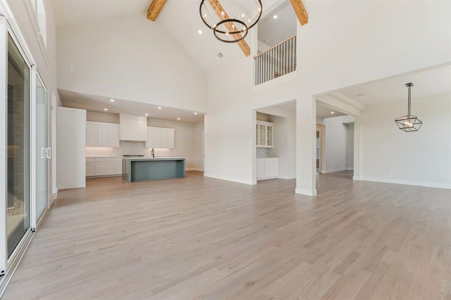 Unfurnished living room with a chandelier, beamed ceiling, light wood-style flooring, high vaulted ceiling, and recessed lighting Unfurnished living room with a chandelier, beamed ceiling, light wood-style flooring, high vaulted ceiling, and recessed lighting