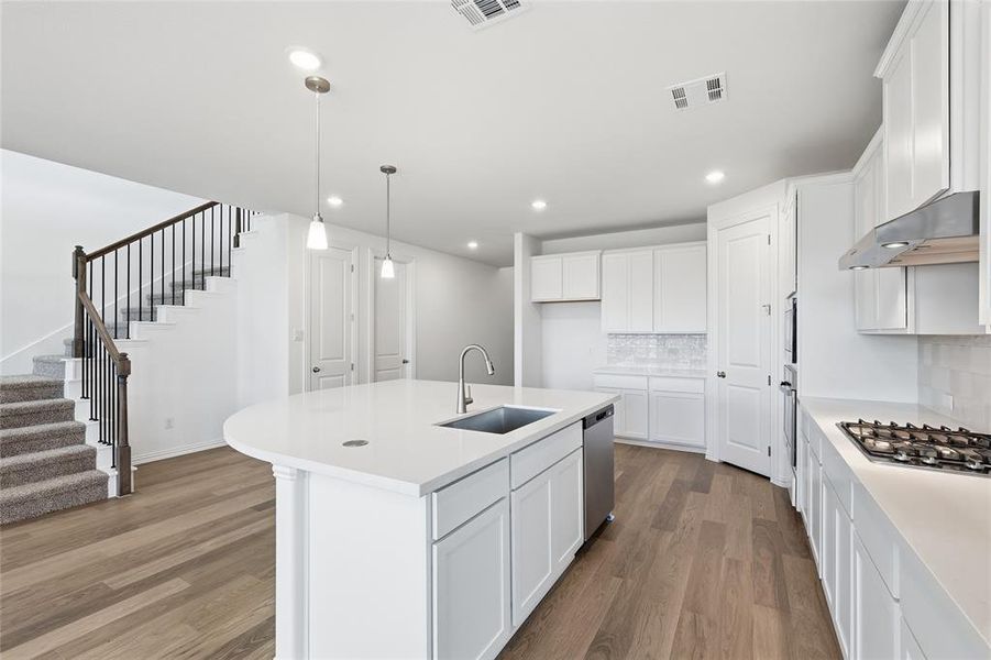 Kitchen featuring a kitchen island with sink, dark wood-style floors, white cabinetry, decorative backsplash, and decorative light fixtures