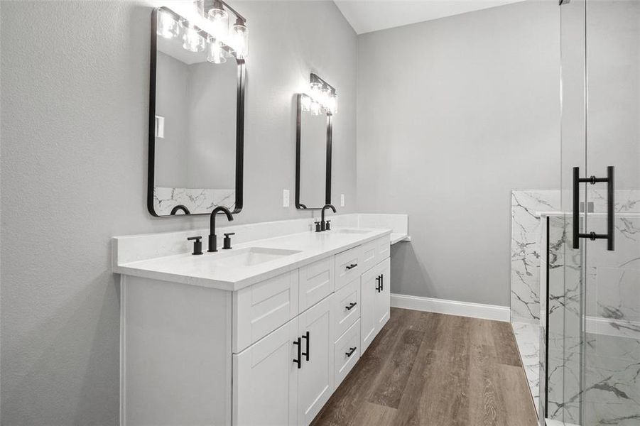 Full bath featuring double vanity, a marble finish shower, and wood finished floors Full bath featuring double vanity, a marble finish shower, and wood finished floors