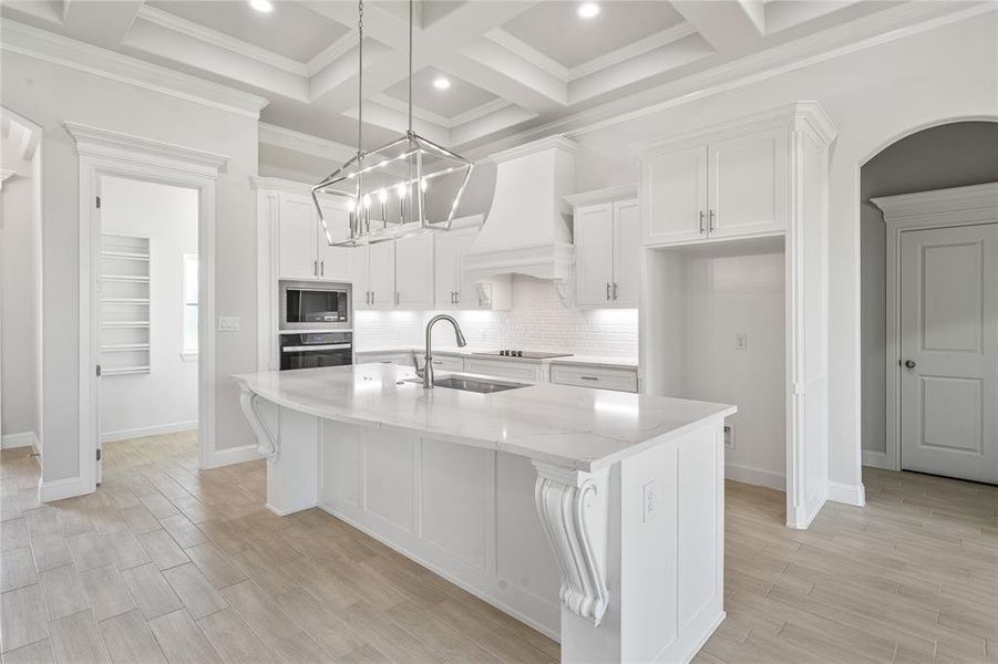 Kitchen with a center island with sink, wood tiled floors, white cabinets, decorative backsplash, and beam ceiling