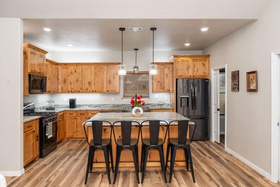 Kitchen featuring a kitchen island, a kitchen bar, hanging light fixtures, black appliances, and light hardwood / wood-style flooring