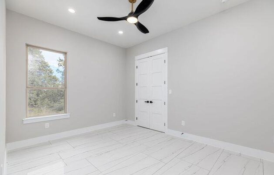 Interior room featuring large format tile flooring, recessed lighting, a modern ceiling fan with brass accents, white baseboards, and a double-door closet with black hardware