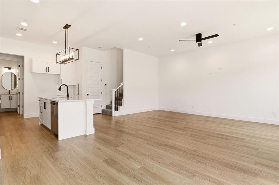 Kitchen with white cabinetry, a ceiling fan, open floor plan, a kitchen island with sink, and light wood-style flooring