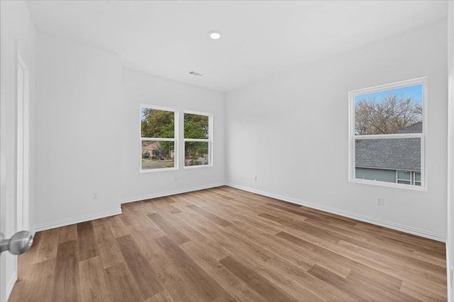 Spacious primary bedroom featuring wood-look flooring, neutral paint, and abundant natural light. Includes a private en-suite bathroom and walk-in closet.