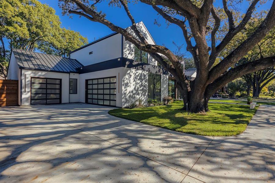View of property exterior featuring a metal roof, a standing seam roof, concrete driveway, a yard, and stucco siding View of property exterior featuring a metal roof, a standing seam roof, concrete driveway, a yard, and stucco siding