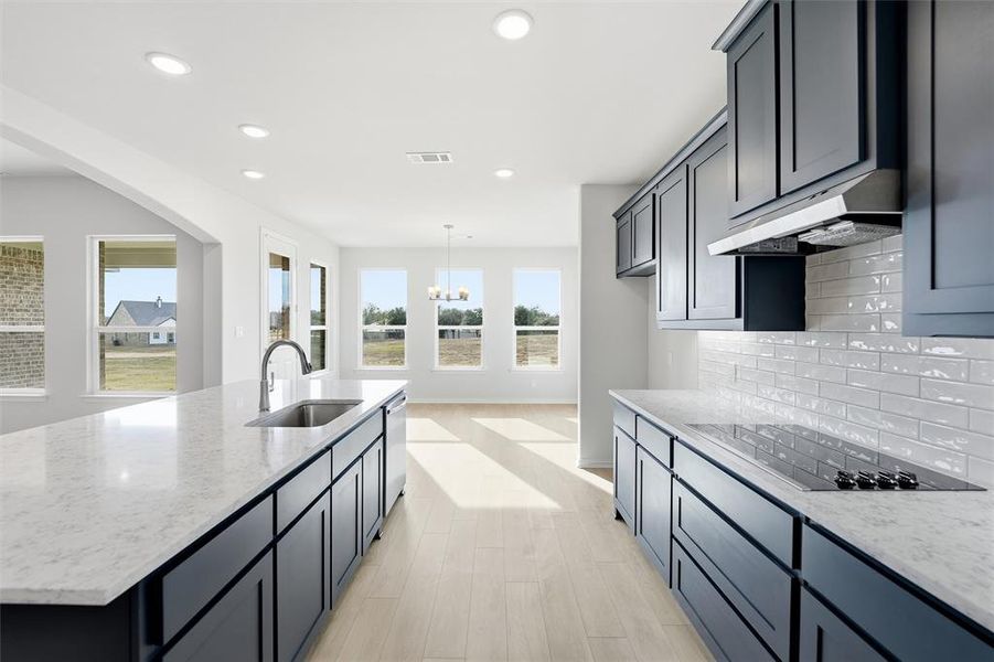 Kitchen with light stone countertops, black electric cooktop, a kitchen island with sink, recessed lighting, and healthy amount of natural light