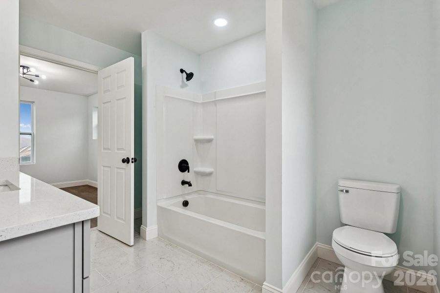 Gorgeous Jack and Jill Bathroom with quartz counter top, tile flooring, elegant lighting, framed mirror and large windows for natural lighting
