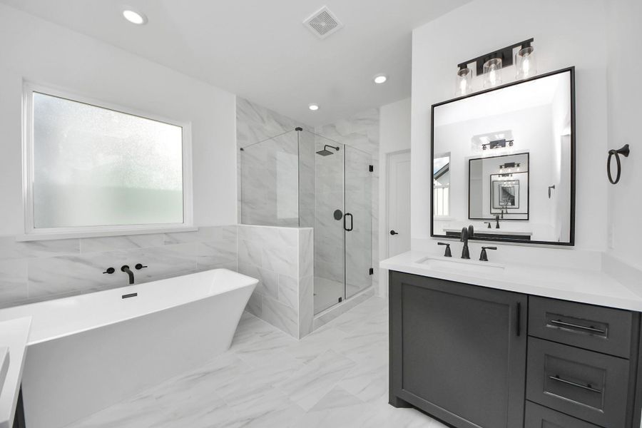 This modern bathroom features a sleek design with a free standing bathtub, a glass-enclosed shower, and stylish fixtures. The space is brightened by natural light from large windows and has elegant marble-like tiles for a luxurious feel.