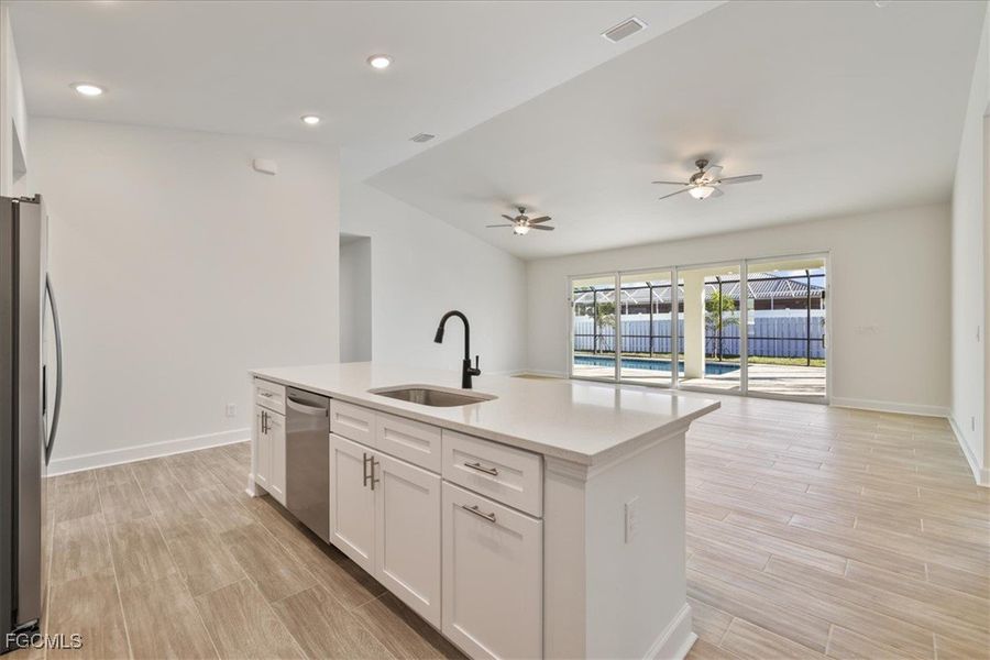 Kitchen featuring white cabinetry, a kitchen island with sink, wood finish floors, stainless steel appliances, and open floor plan