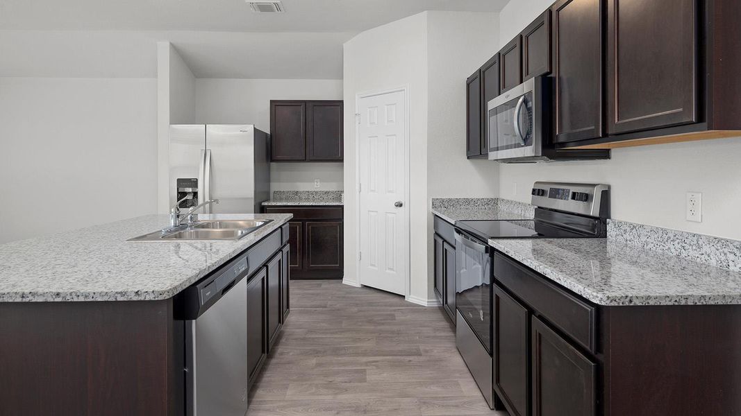 Kitchen featuring stainless steel appliances, dark wood finish cabinets, a center island with sink, and light wood-type flooring