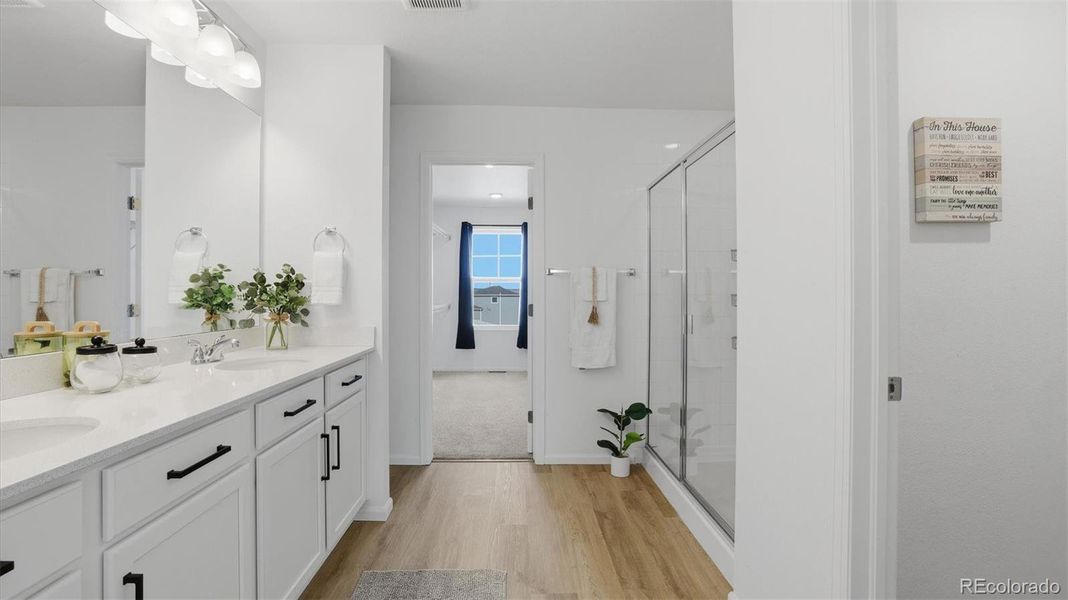 Upper Level Primary Bathroom with dual sink vanity, mirror, luxury vinyl plank flooring and enclosed tiled shower.