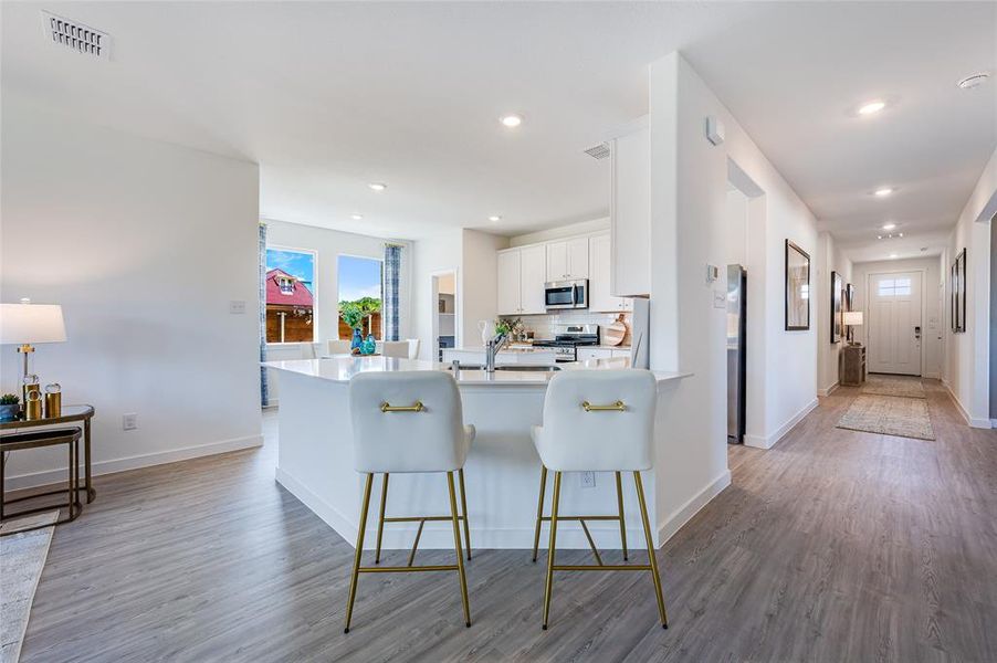 Kitchen with a kitchen breakfast bar, appliances with stainless steel finishes, light hardwood / wood-style floors, white cabinetry, and kitchen peninsula