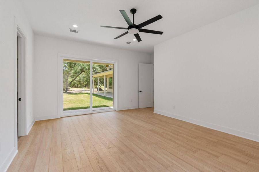 A well-lit bedroom features light wood flooring and sliding glass doors that open to a verdant outdoor space.
