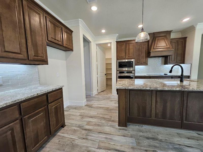 Kitchen featuring decorative backsplash, light stone counters, premium range hood, decorative light fixtures, and stainless steel appliances