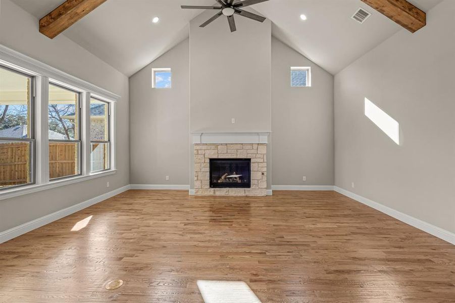 Unfurnished living room with a stone fireplace, high vaulted ceiling, beam ceiling, and light hardwood / wood-style flooring