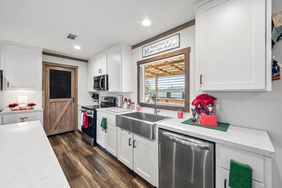 White cabinetry with dark hardware, wood-finish flooring, and a farmhouse sink