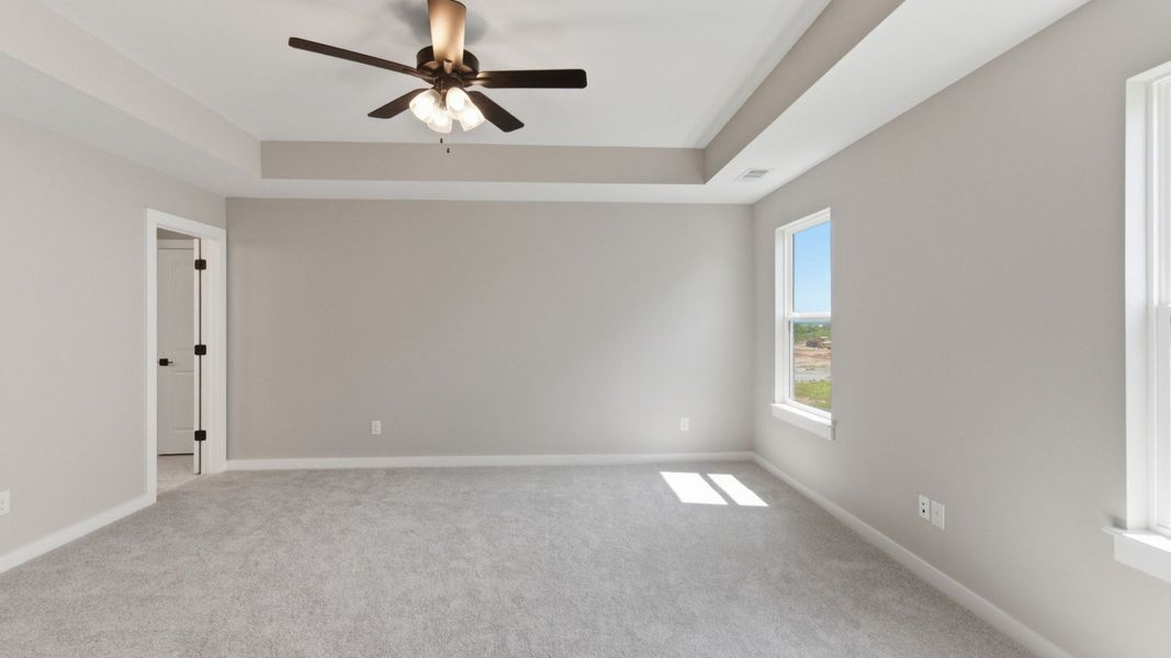 Primary suite with tray ceiling, ceiling fan, and carpet