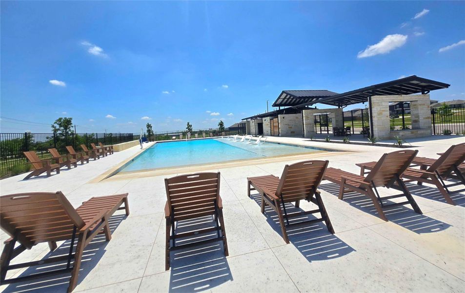 Resort-style pool area featuring a large swimming pool, expansive paved decking, and a shaded pavilion with stone elements