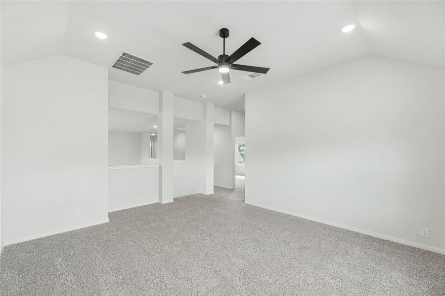 Empty living room with gray carpet, white walls, vaulted ceiling, and black ceiling fan