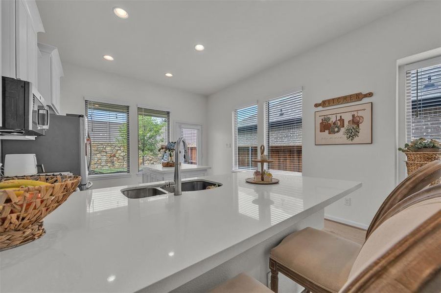 Contemporary kitchen featuring a large white countertop island with an undermount dual-basin sink and stainless steel faucet Contemporary kitchen featuring a large white countertop island with an undermount dual-basin sink and stainless steel faucet