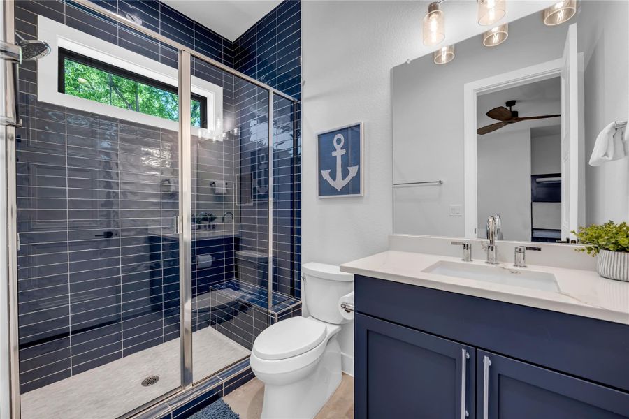 Bathroom three: Modern bathroom featuring a glass-enclosed shower with dark blue rectangular tiles and a built-in bench