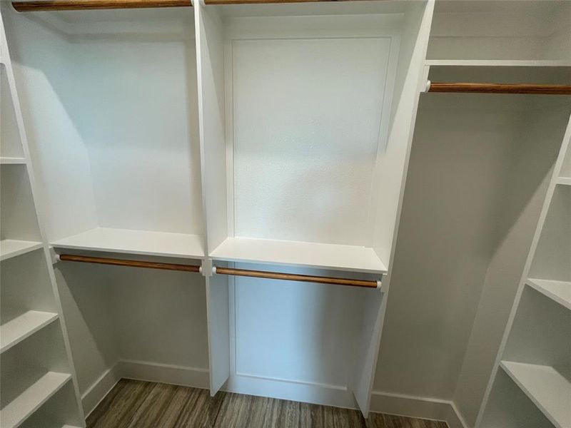 Custom closet system featuring white built-in shelving, wood-finish hanging rods, and wood-finish flooring