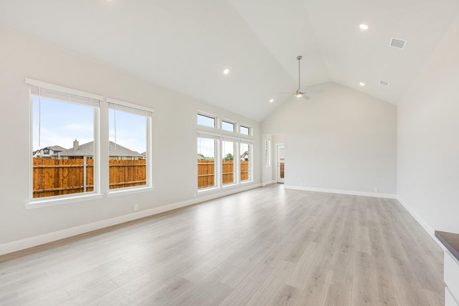 Open living room with vaulted ceiling, light wood floors, and large windows overlooking backyard fence