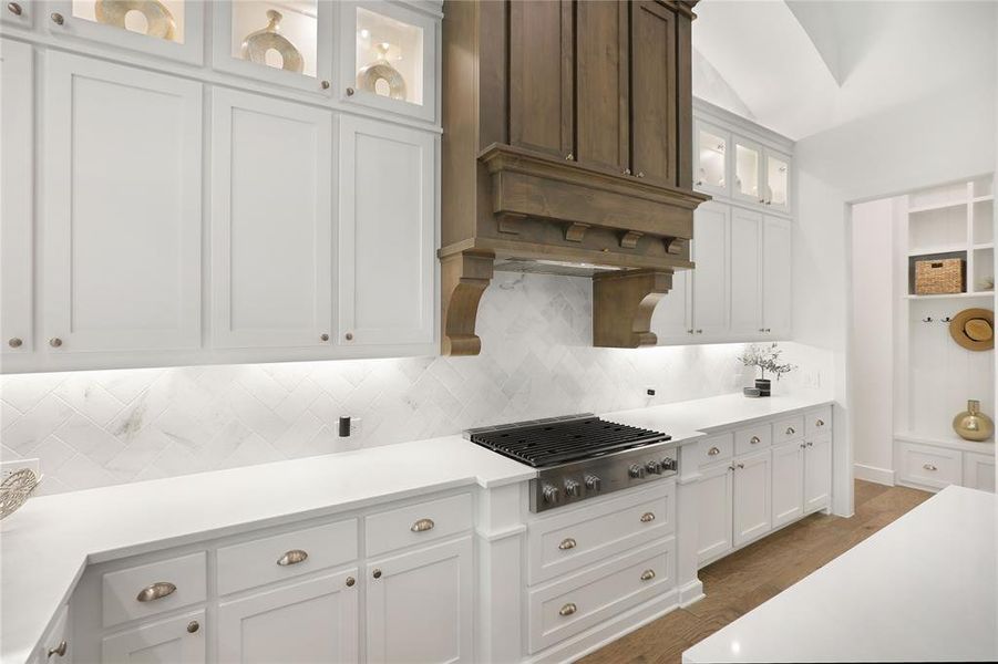Gourmet kitchen featuring a wood range hood, white flat-panel cabinetry, white countertops, and a full-height chevron pattern backsplash